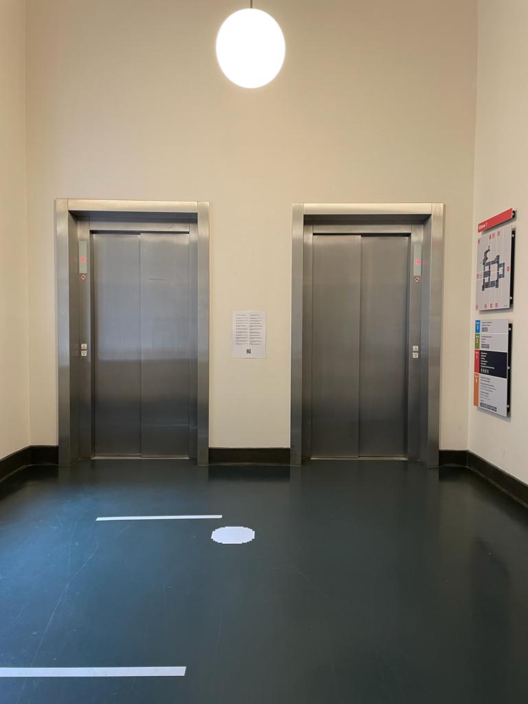 Photo of two elevators with closed metal doors at the end of a hallway.