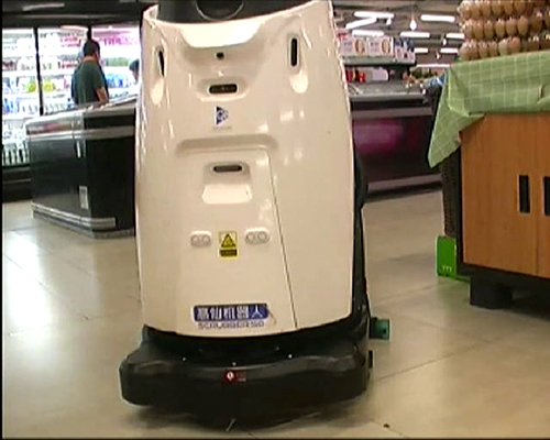 Video still showing a black and white cleaning robot in a supermarket. It resembles a pinguin.