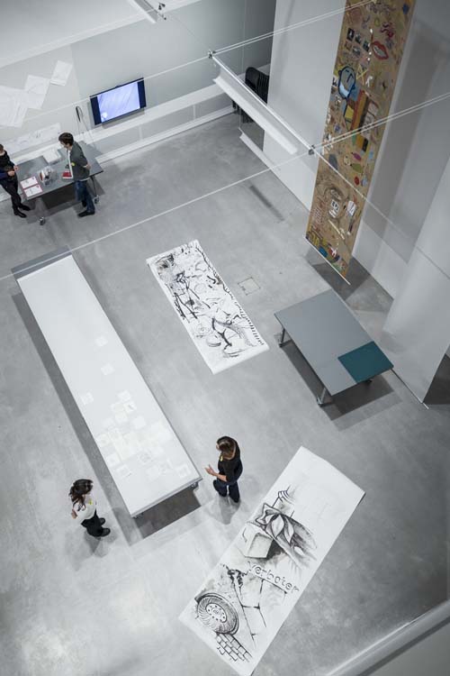 Birds-eye view of a big hall in Berlinische Galerie with long paper banners on the wall, the floor and a table.