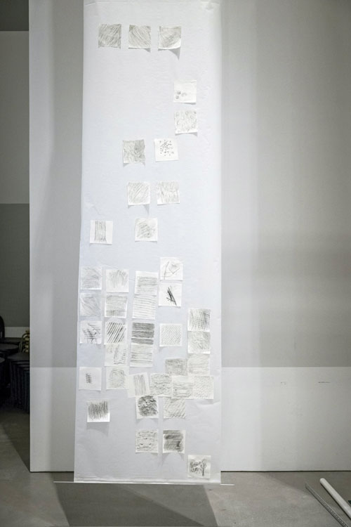 Close-up of a long piece of paper hanging from the ceiling with many small frottage drawings mounted on it.